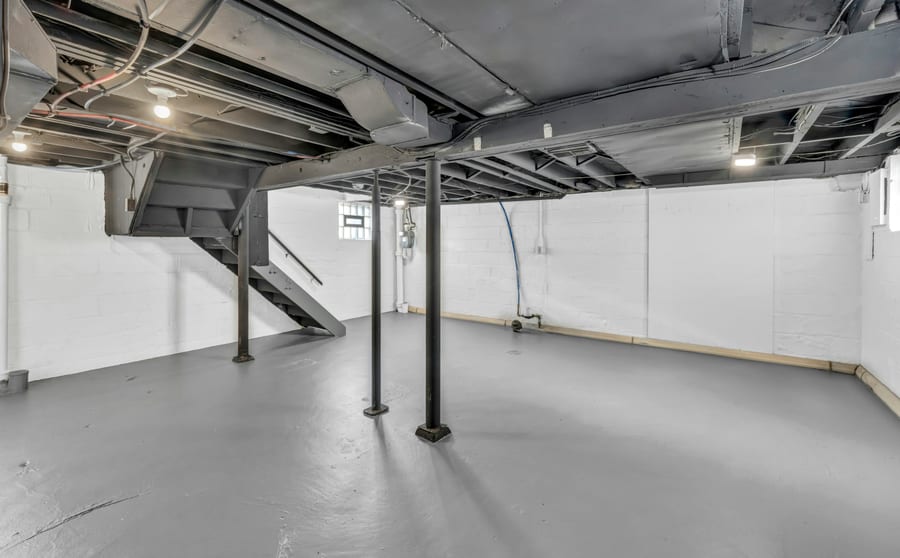 An empty painted basement with steel columns, exposed ductwork and a bare floor