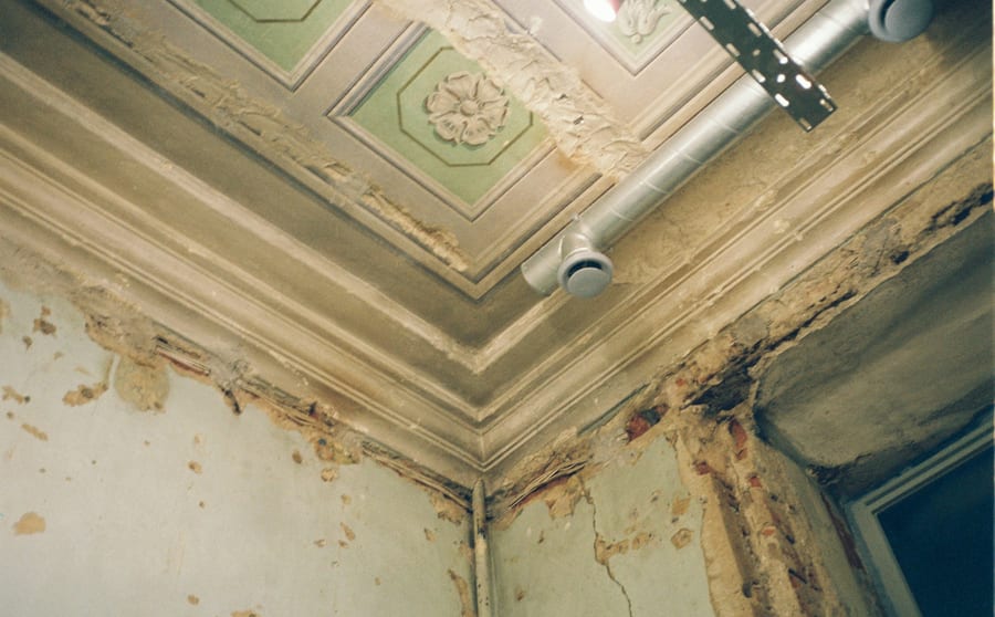 A decorated ceiling and cornice with the plaster blown and the paint peeling away in one corner