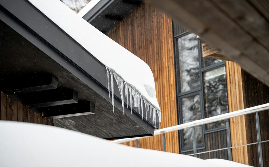 Icicles hanging from the eave of a snow-loaded roof on a timber-clad building