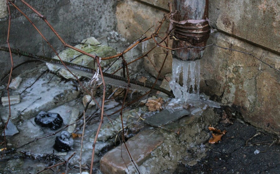 Ice built up around the foot of an old pipe against a stone wall