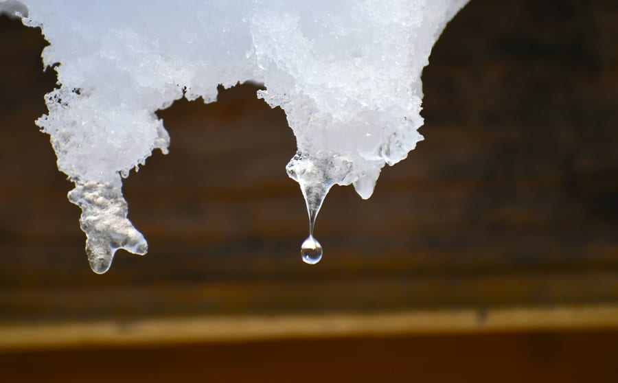 Melting snow on a timber edge with a drop of water about to fall